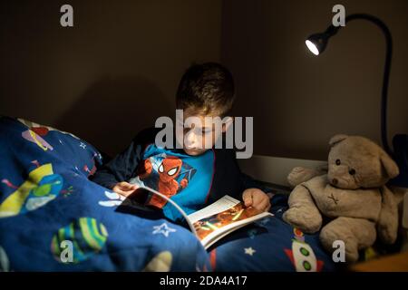 6 year old boy reading whilst lying in bed at bedtime at home, England, United Kingdom Stock Photo