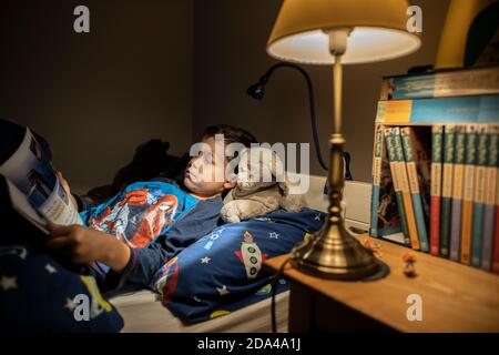 6 year old boy reading whilst lying in bed at bedtime at home, England, United Kingdom Stock Photo