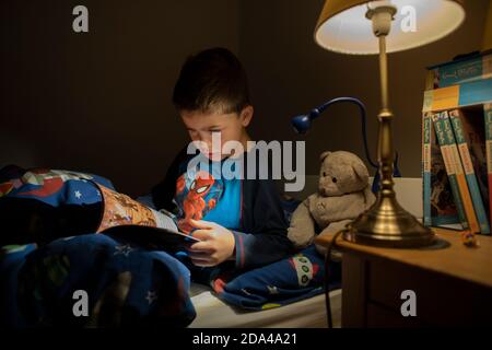 6 year old boy reading whilst lying in bed at bedtime at home, England, United Kingdom Stock Photo