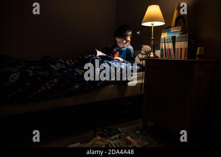 6 year old boy reading whilst lying in bed at bedtime at home, England, United Kingdom Stock Photo