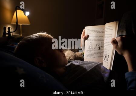 9 year old boy reading whilst lying in bed at bedtime at home, England, United Kingdom Stock Photo