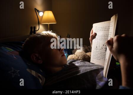 9 year old boy reading whilst lying in bed at bedtime at home, England, United Kingdom Stock Photo