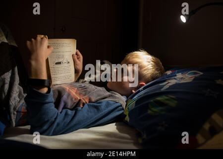 9 year old boy reading whilst lying in bed at bedtime at home, England, United Kingdom Stock Photo