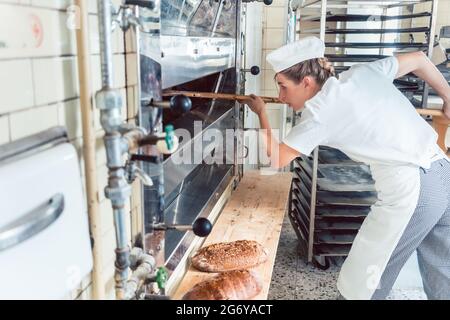 Baker woman getting bread out of bakery oven in her bakery Stock Photo