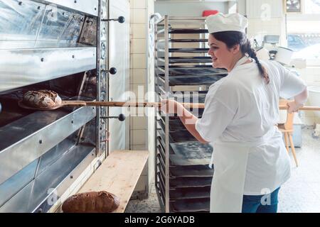 Baker woman getting bread out of bakery oven in her bakery Stock Photo