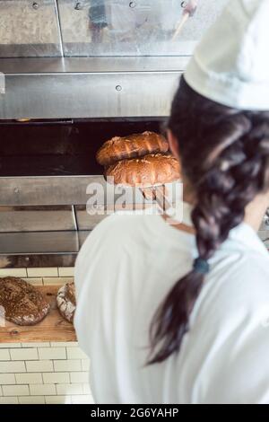 Baker woman getting fresh bread with shovel out of oven Stock Photo