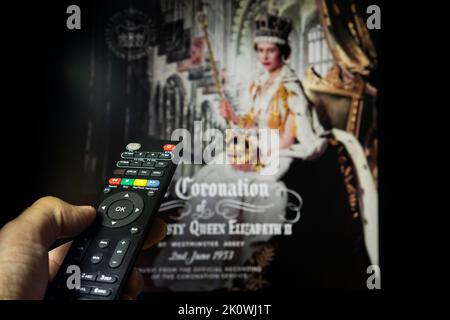 Belgrade, Serbia - September 12, 2022: Queen Elizabeth II coronation. Watching documentary about Queen of England on tv with remote controle in hand. Stock Photo