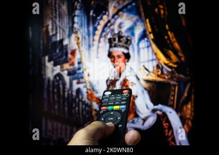 Belgrade, Serbia - September 12, 2022: Queen Elizabeth II coronation. Watching documentary about Queen of England on tv with remote controle in hand. Stock Photo