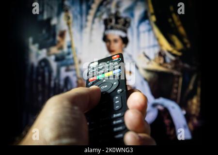 Belgrade, Serbia - September 12, 2022: Queen Elizabeth II coronation. Watching documentary about Queen of England on tv with remote controle in hand. Stock Photo