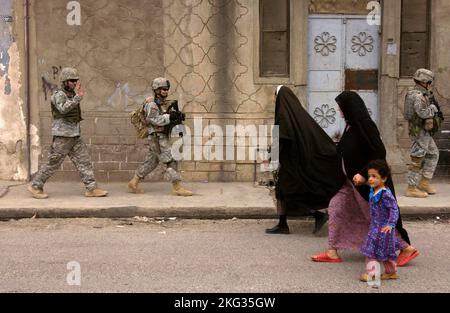 MOSUL, IRAQ - 12 April 2006 - US Army soldiers wave and smile as they pass by two Iraqi women and a child during a neighborhood foot patrol in Mosul, Stock Photo