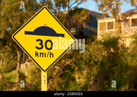 A sign indicating a speed bump ahead, advising to slow down and drive at a 30 kilometres an hour speed limit on a suburban street, Western Australia. Stock Photo