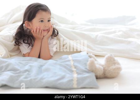 Girl under duvet on bed playing with stuffed animal Stock Photo