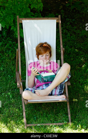 Child, boy, 11 years, reading a exciting holiday book whilst sitting in a deck chair in the garden Stock Photo