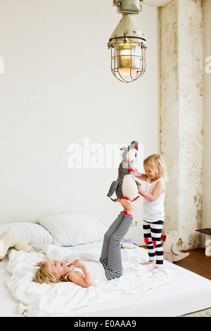 Young sisters playing with soft toy on the bed Stock Photo