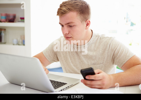 Teenage Boy Sending Text Message Whilst Studying On Laptop Stock Photo