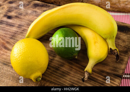 Fresh and ripe citrus fruits, lemon and lime, together with bananas on cutting board. Stock Photo