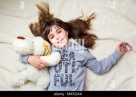 Cute little girl hugging her toy lying on bed Stock Photo