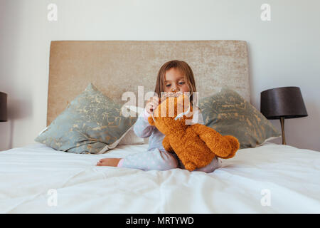 Cute little baby girl putting a crown on her teddy bear. Innocent girl child playing with her soft toy. Stock Photo