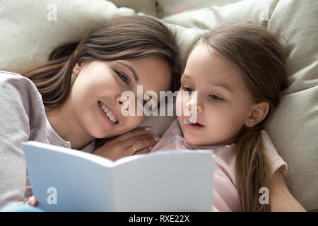 Happy mom listening child daughter learning reading book in bed Stock Photo