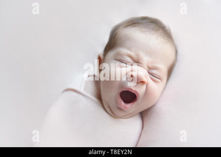 Newborn baby girl yawning lying in a pink blancket Stock Photo