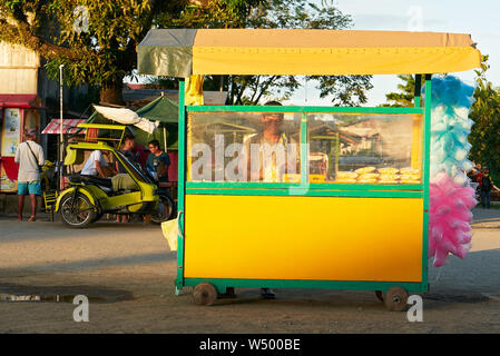 Cuartero, Capiz Province, Philippines: Young man selling popcorn and colorful cotton candy in a small yellow push cart late afternoon Stock Photo