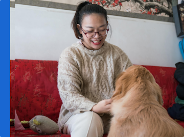 A woman is seated on a couch petting an off-duty guide dog