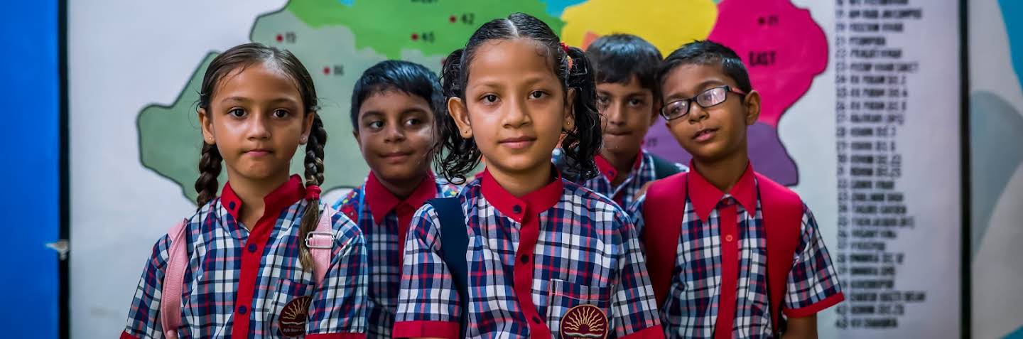 A group of confident school children in uniform standing in front of a map.