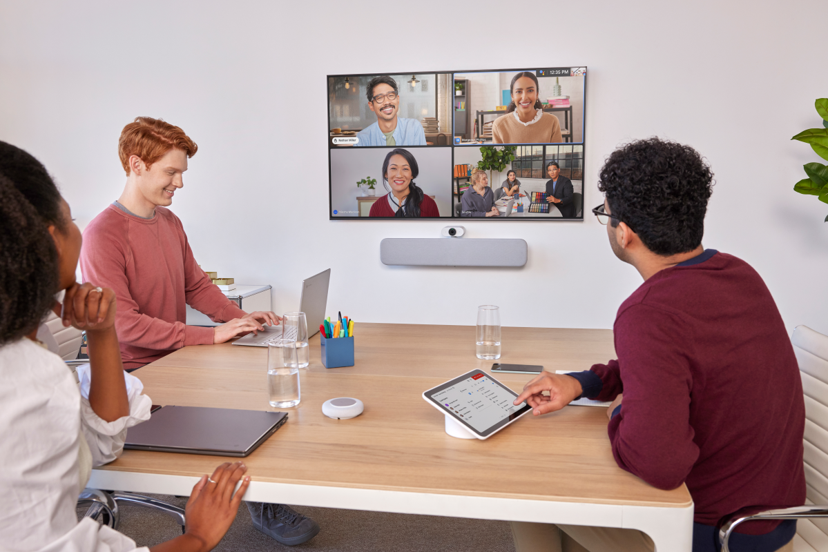 Una sala de reuniones con tres personas y otras cuatro conectadas online en una videoconferencia