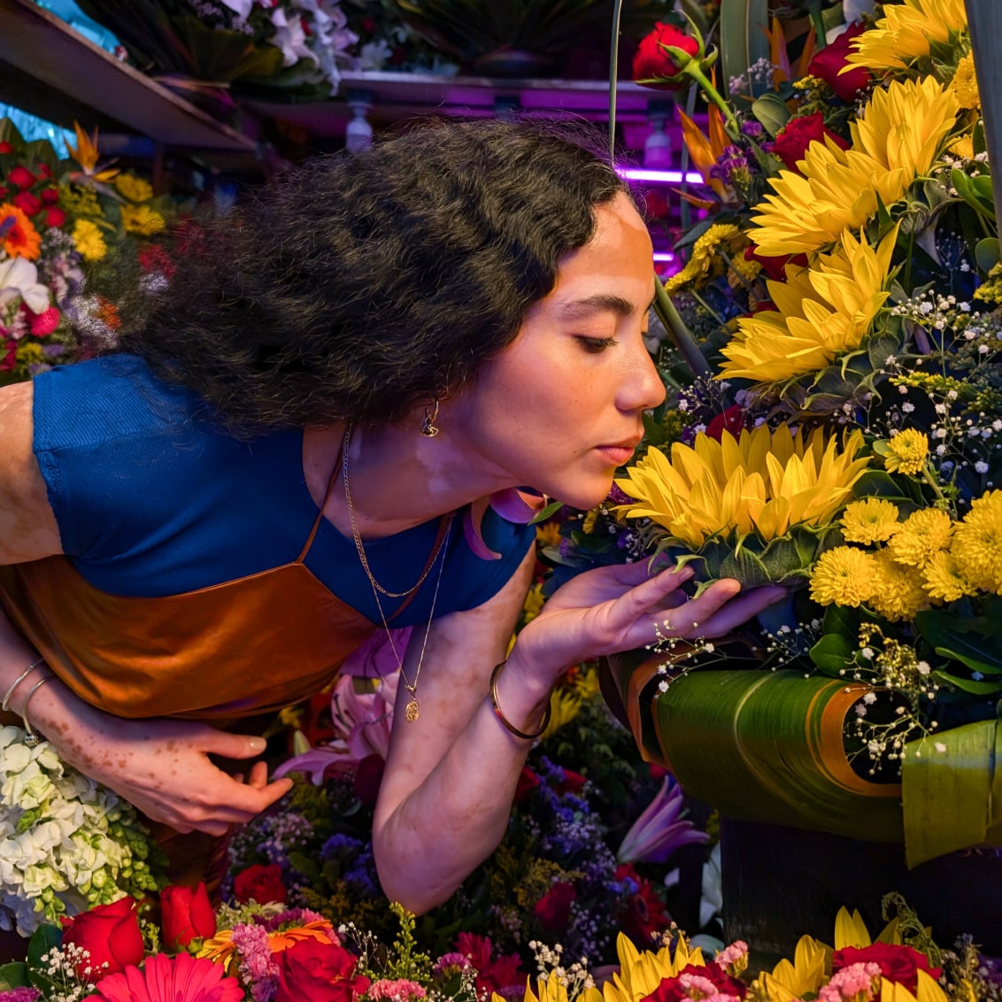 A person surrounded by flowers poses for a photo. They hold a flower in their hand. Pixel 9 Pro works to beautifully capture the colors and skin tones in the photo.