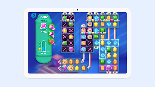 Une tablette affiche le jeu Candy Crush Soda Saga avec des pailles, des bonbons et le score.