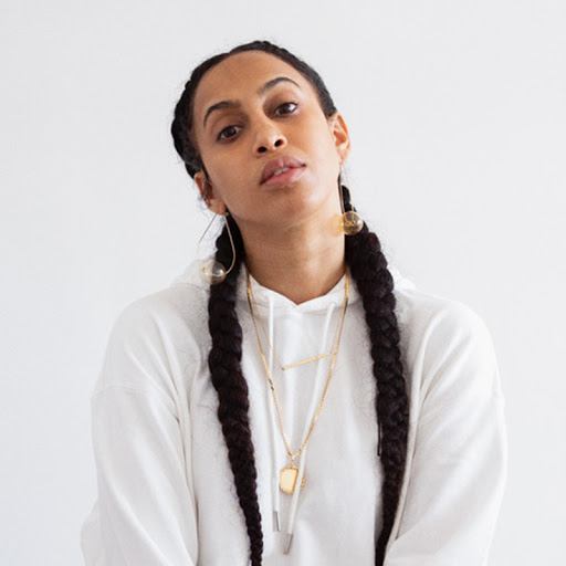 Portrait of artist wearing a white hoodie and two long french braids.