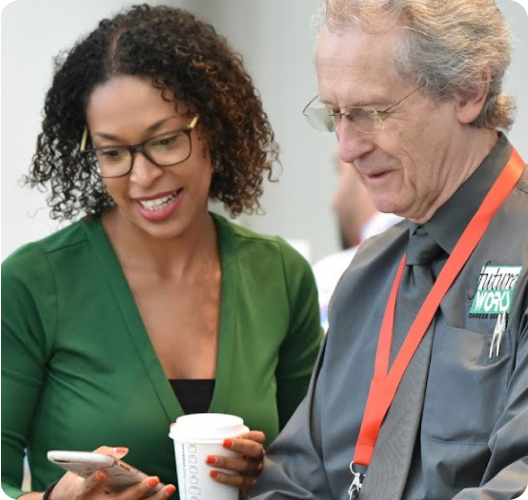 A woman shows a man something on her phone. The woman is smiling.