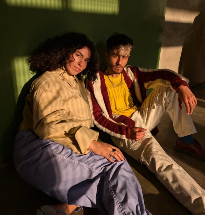 Two people pose seated against a wall in dim light.