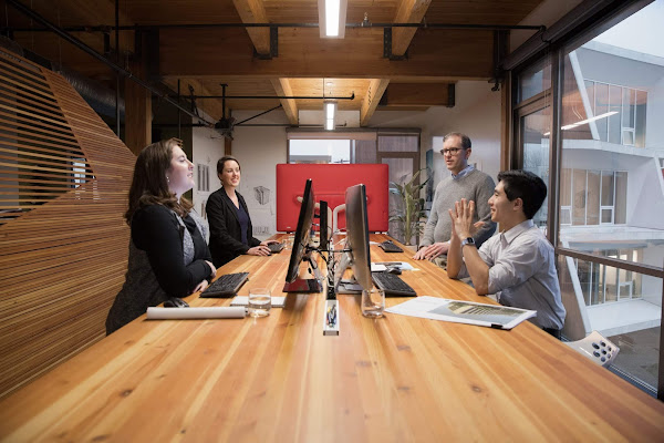 Administradores de TI falando em frente a uma mesa com computadores no meio