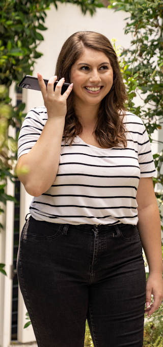 A woman standing in a back garden holding up her phone to hear the speaker's sounds.