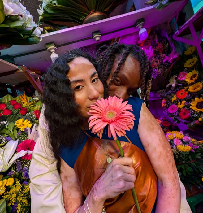 Two people pose facing the Pixel Camera, surrounded by flowers. Colors and skin tones are vividly captured by Pixel 9.