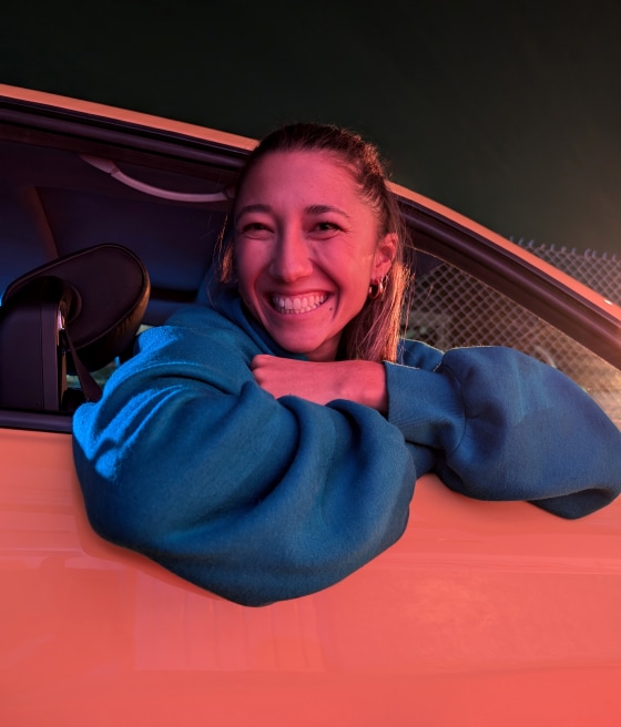 A person leans out of a car, smiling, in dim pink light.