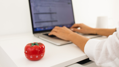 Person at laptop with a red pomodoro timer on the desk next to them