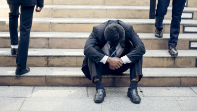 Man in business suit sitting on office steps, slouched over in sadness or frustration