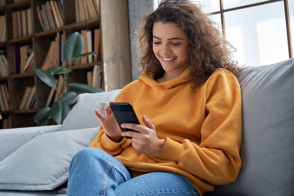 Teenage girl sitting on couch and using phone securely