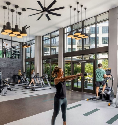 A woman is doing exercises in a gym with a ceiling fan