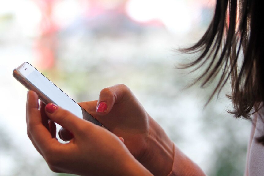 Anonymous hands with red-painted nails holding a phone. 