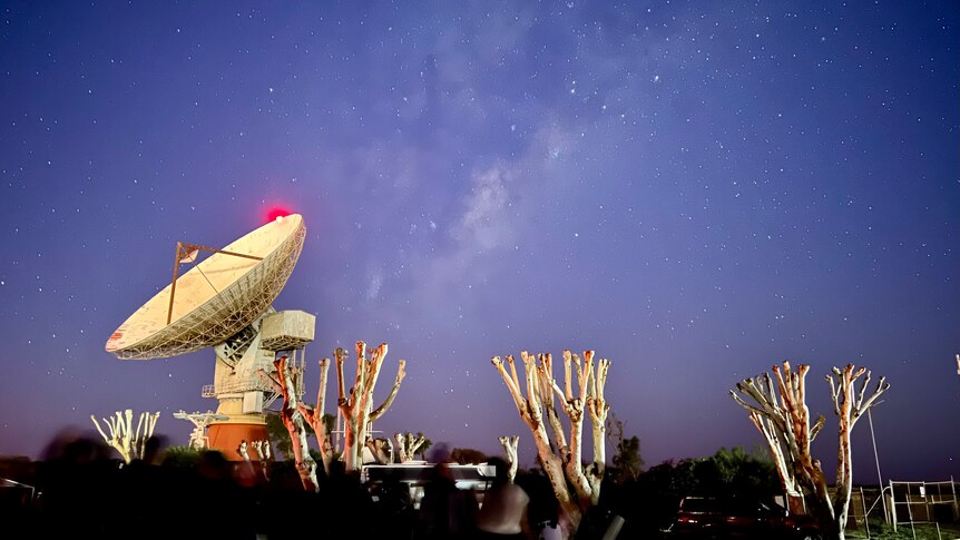 A large rocket and satellite dish point upwards into the evening sky.