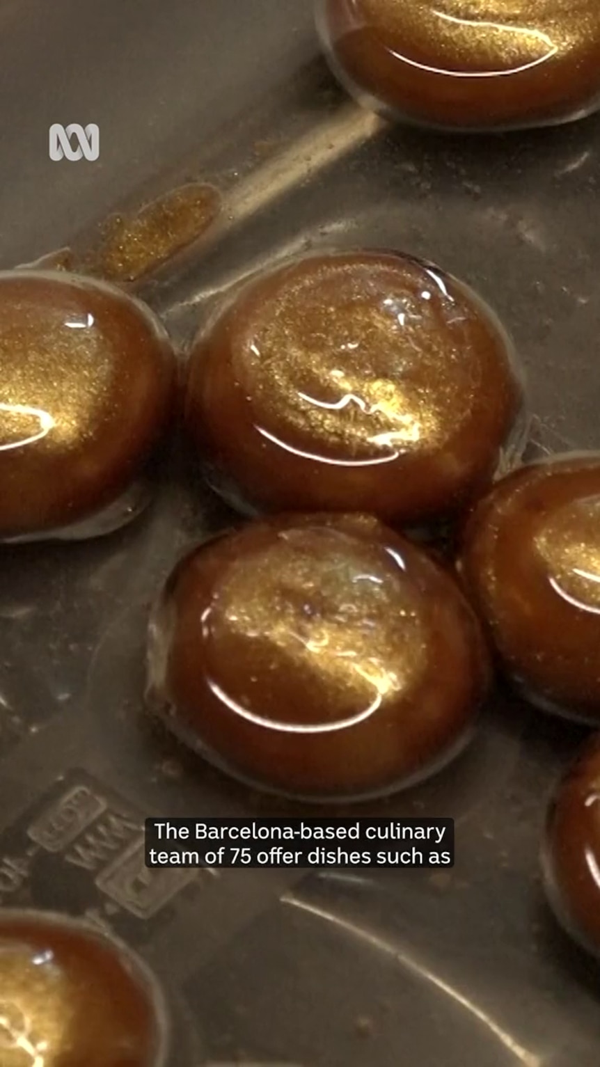 Shiny golden globules sit in a clear substance in a metal vessel 