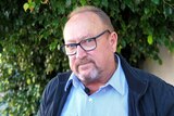 Older man with glasses and a blading head standing outdoors