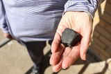 A woman's hand holding a piece of meteorite that looks like a black rock.