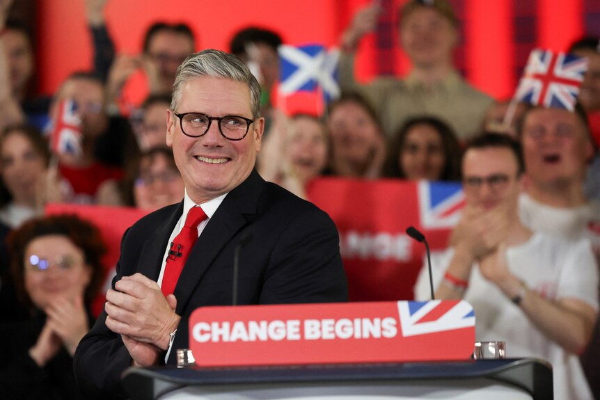 Keir Starmer claps his hands together as a crowd behind him cheers.