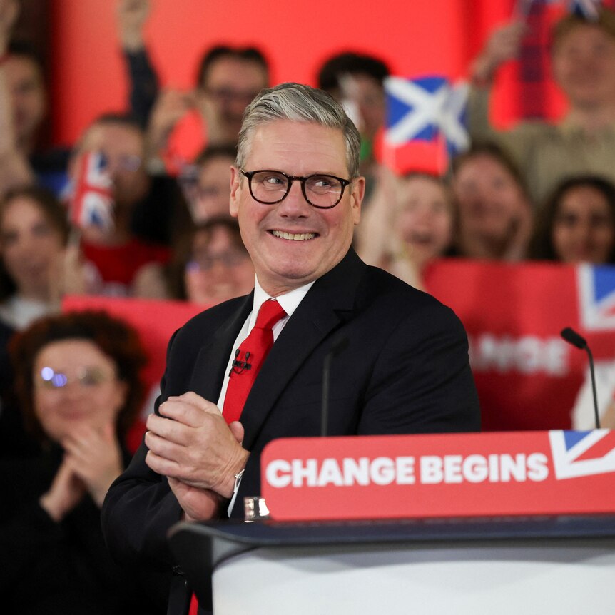 Keir Starmer claps his hands together as a crowd behind him cheers.