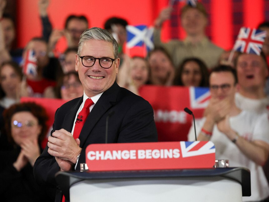 Keir Starmer claps his hands together as a crowd behind him cheers.