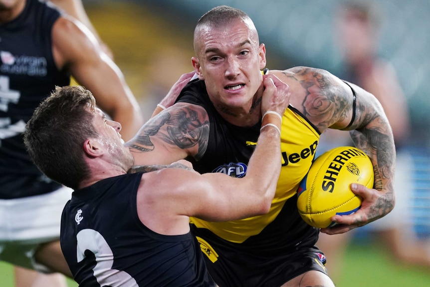 AFL player grips ball in one hand while sticking his arm out to keep away from an opposition tackle.